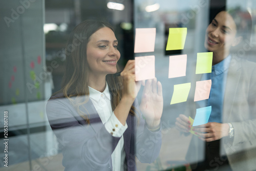 Schilderij op canvas Two businesswomen collaborating on a project using sticky notes on a glass wall