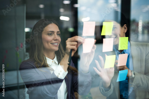 Foto Two women collaborating on a glass wall with colorful sticky notes for brainstor
