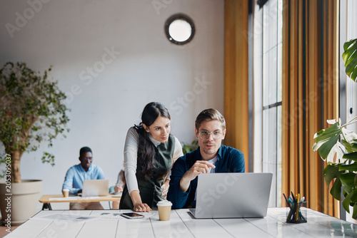 Business people collaborating on a laptop in a modern office, young male and female colleagues brainstorming ideas and working together on a new project, showing teamwork and consultation
