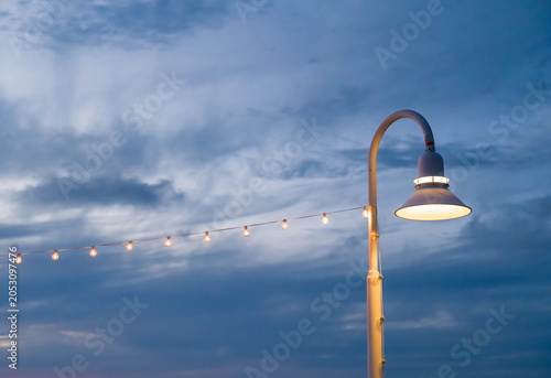 Fotografie White metal street lampposts and the decorative string lights hang over the Key West town area near the tropical ocean coast
