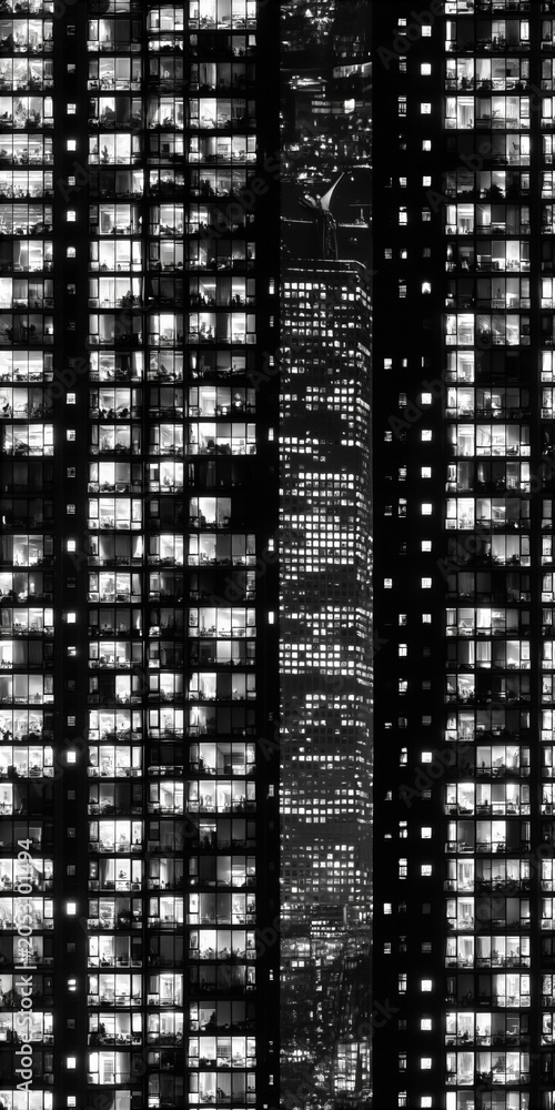 Fototapeta premium Monochromatic high rise building facade at night with glowing windows creating a symmetrical urban geometric pattern
