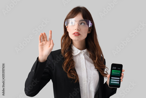Young businesswoman in AR glasses with mobile phone using virtual screen on g...