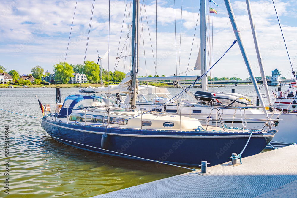 Obraz premium Sailboats docking at pier on sunny day with bridge in background