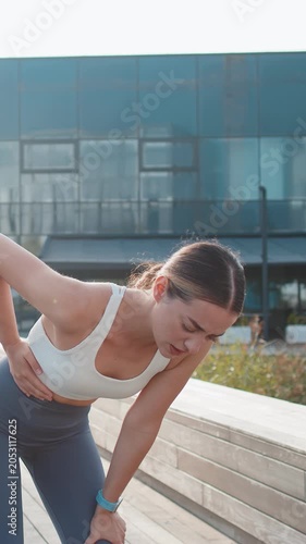 Young Caucasian runner suffering from abdominal pain during a run in urban city park on sunny day. Sad woman keeps her hand on her stomach. Girl has poisoning, constipation, spasms or menstruation.