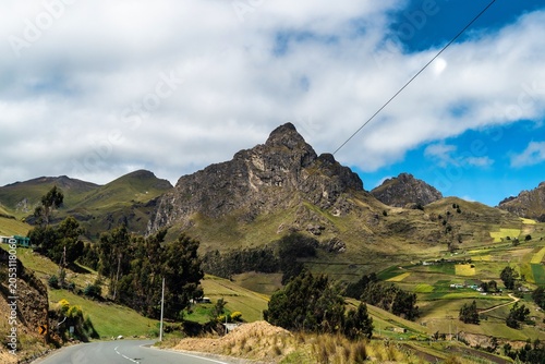 Fotografie Mountains Rise Over a Winding Road in the Countryside With Fields and Trees Unde