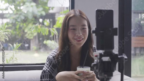 Female creator recording matcha review livestream. Cozy indoor cafe setting with sunlight through window, smartphone on tripod