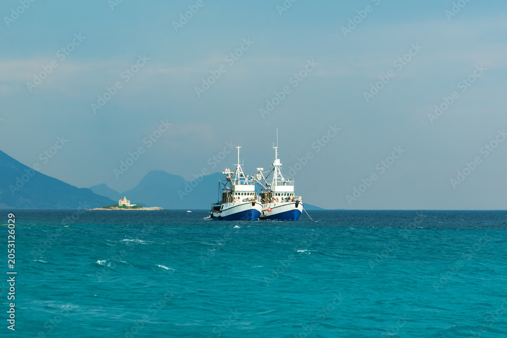 Obraz premium Croatian twin fishing trawlers preparing for a catch in clear turquoise waters near the Peljesac peninsula with lighthouse on the background, Croatia