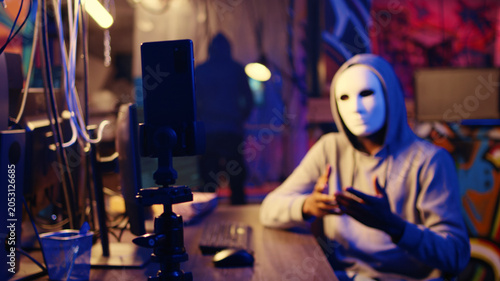 Photos Hacker wearing anonymous mask threatens victim with deploying malware designed to exploit network backdoors if his demands are not met, filming ransom video after bypassing security measures