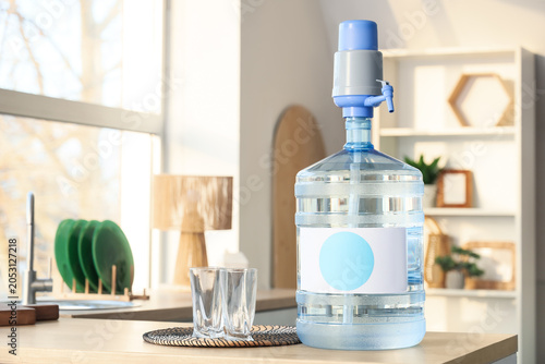 Tableau sur toile Bottle of clean water with glasses on table in kitchen