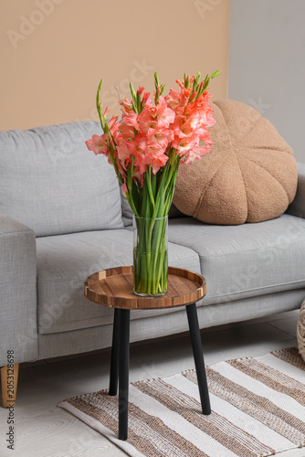 Vase with gladiolus flowers on table near sofa in living room