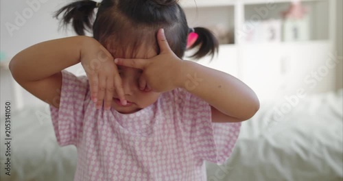 Sleepy Asian Toddler Girl Rubbing Eyes in Minimalist Room; Two Year Old Child Tired After Playing, Looking Drowsy in Cute Medium Shot Portrait, Childhood Fatigue and Bedtime Routine.