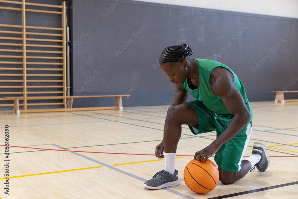Naklejka premium Orange basketball is sitting beside gray sneakers on hardwood court with painted lines at gym