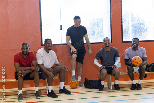Fotografía Diverse male teammates in sportswear sitting on gym bench, holding basketballs n