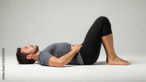 A man lies on his back with bent knees and hands on his stomach, performing a relaxation or core exercise on a light background.