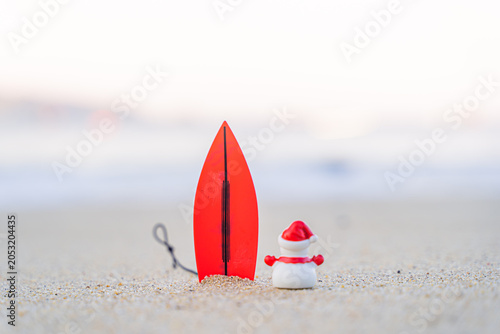 Sandy Christmas Snowman is watching the waves, standing on beautiful beach with a surf board - horizontal version in Patong Beach, Phuket, Thailand
