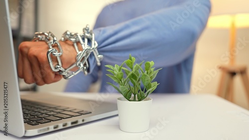 Foto A person with a chained fist raised toward a laptop reflects the frustration, rebellion, or anger from feeling trapped by technology, stress, digital overload, burnout, and the urge to break free