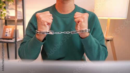 Tableau sur toile A freelancer sits at a desk in handcuffs before a laptop, symbolizing feeling trapped at work