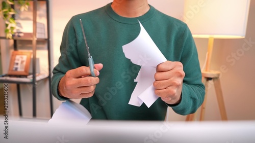 Fotografia An office worker angrily cuts a sheet of paper with scissors in front of a laptop, expressing frustration