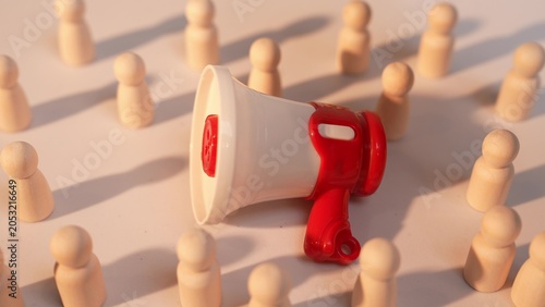Photography A hand places a small megaphone surrounded by many wooden figurines, symbolizing mass communication, the spread of ideas, collective influence, and the role of leadership in guiding communities