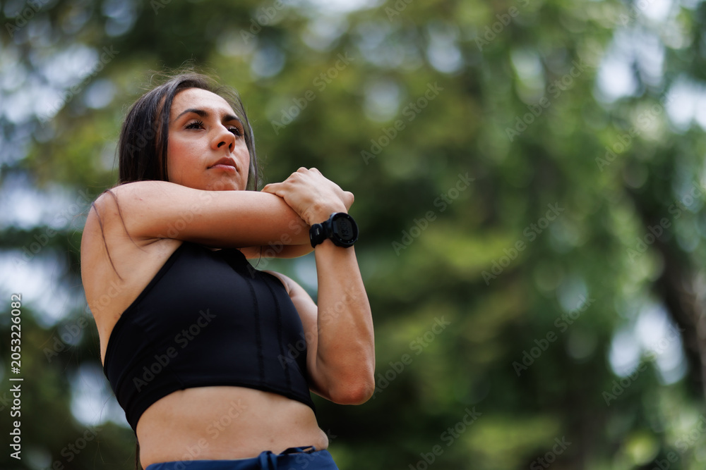 Naklejka premium Young woman in athletic wear stretching arms outdoors in a natural green environment