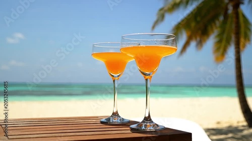 Two orange cocktail glasses standing on wooden table on beautiful tropical resort beach