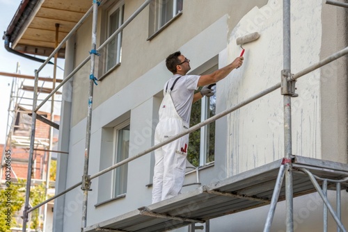 Man paints exterior wall with paint roller