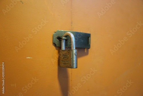 Canvas-taulu Close up of an old brass padlock locked on a metal latch against an orange wall