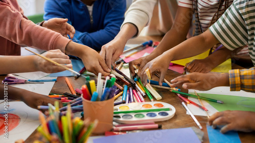 Close-up of children sharing colorful art supplies during a creative classroom craft activity, emphasizing teamwork and learning.