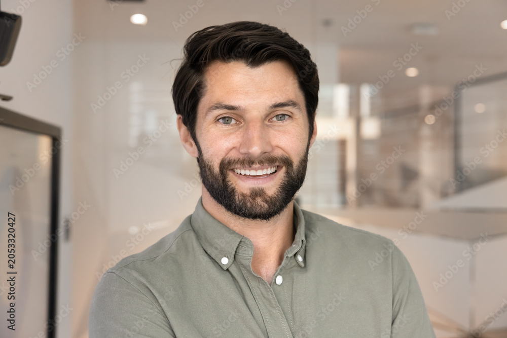Obraz premium Head shot close up portrait of confident bearded man smiling at camera standing in modern office, representing professionalism, success and leadership in business. Company boss, or CEO profile picture