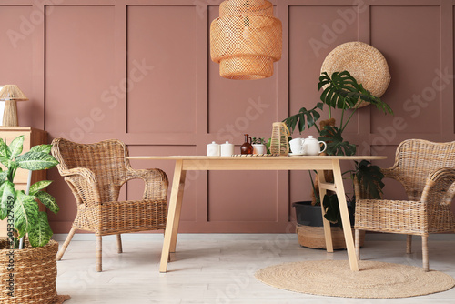 Foto Boho chic dining room interior with wicker furniture, wooden table, and housepla
