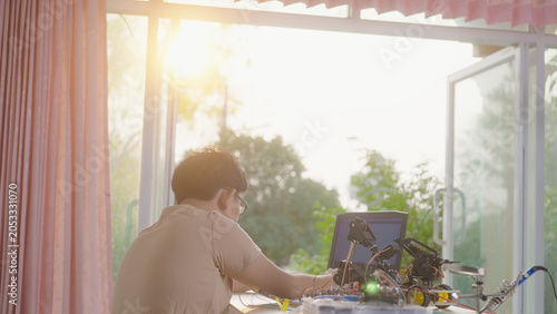 Asian young student using a laptop at home while working on a robotics project with electronic components and robotic devices. Concept of STEM education, coding, and technology learning.