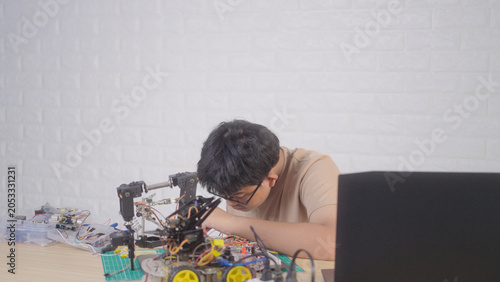 Asian young student using a soldering iron for electronics and robotics projects at home with robotic equipment and a laptop. Concept of STEM education, engineering skills, and innovation.
