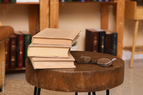 Stack of old books and reading glasses on a rustic wooden stool in a cozy hom...