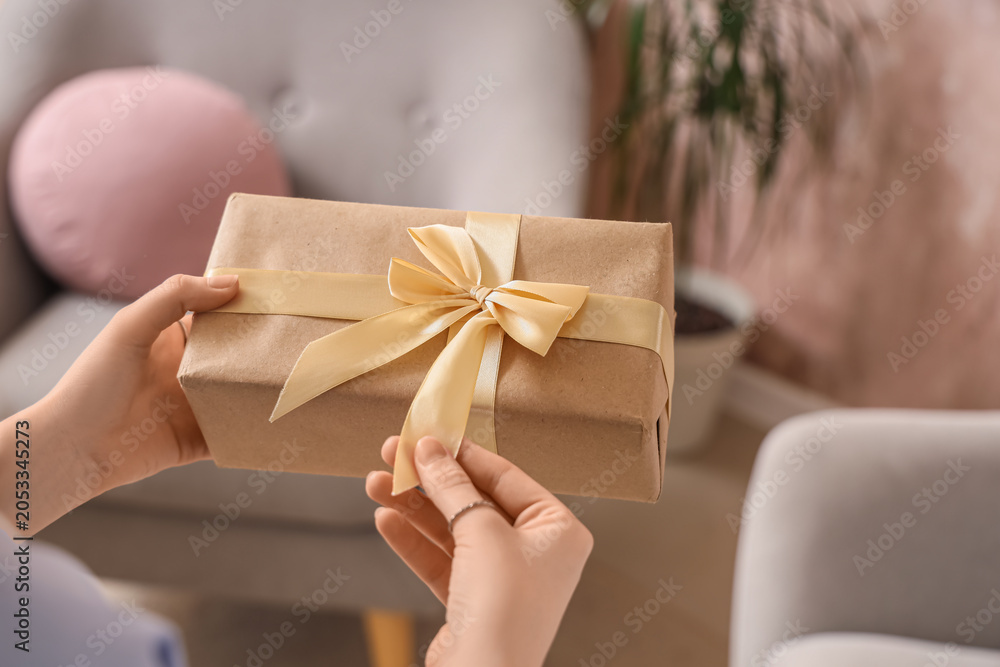 Fototapeta premium Hands untying golden ribbon on brown kraft paper gift box, holiday celebration and special occasion present, the act of unwrapping a gift evokes joy and anticipation