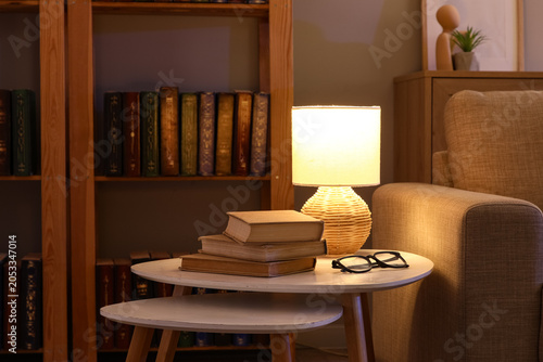 Tableau sur toile Cozy home interior with bookshelf, reading lamp, stack of books, and eyeglasses