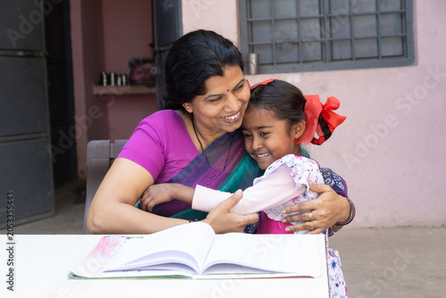 Indian mother and daughter sharing a loving embrace while studying together, rural india education, family bonding, and support in learning.