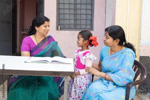 Indian educator and mother sitting with a girl child, childhood learning and development outdoor, educational support in rural india.