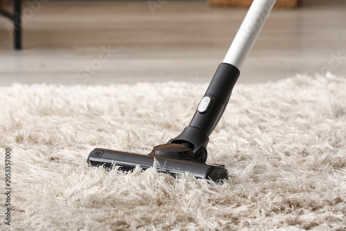 Fotografi Modern vacuum cleaner head cleaning fluffy white shag carpet in a home living ro
