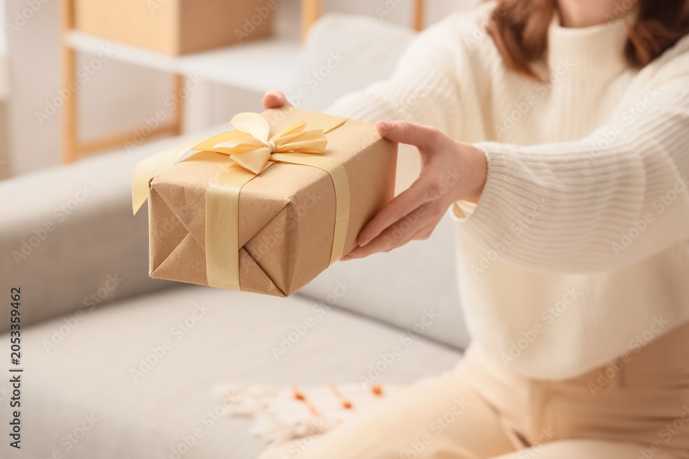 Fototapeta premium Woman in cozy sweater offering a beautifully wrapped gift box with golden ribbon, celebrating holidays and special occasions