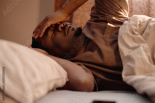 Foto Close up of young adult Black man lying in bed, covering eyes and struggling with screen fatigue after device use at home