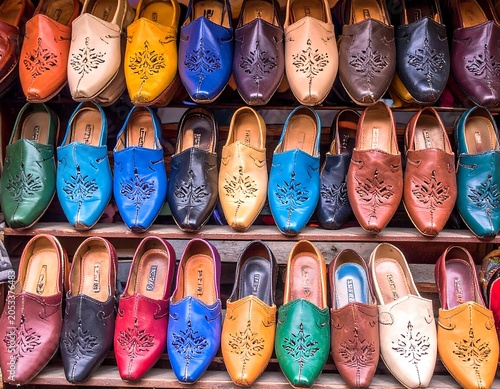 Rows of brightly colored, leather, slip-on shoes with decorative cutouts. Displayed on wooden shelves