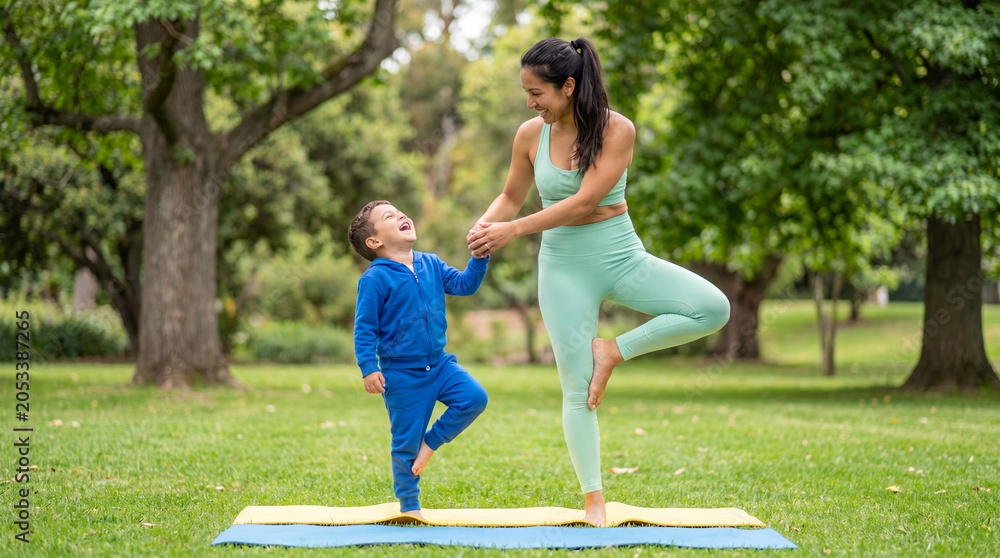 Obraz premium International Yoga Day mother son balance pose holding hands outdoor park joyful playful wellness fitness healthy lifestyle family bonding fun exercise