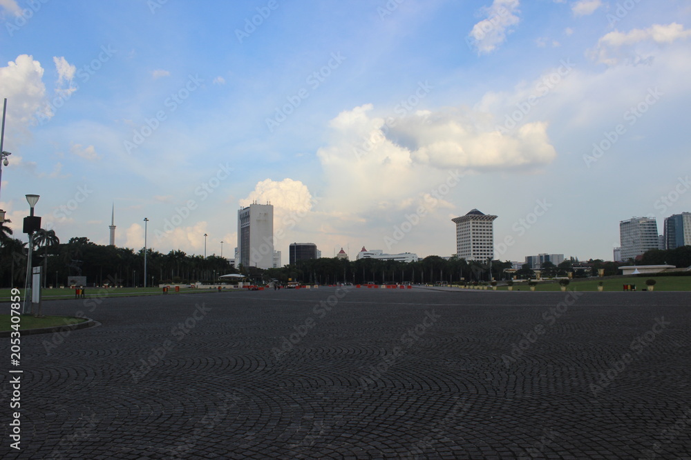 Fototapeta premium Wide urban square paved with stone bricks under cloudy blue sky during daytime.