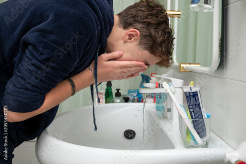 Teenage boy washing his face in the bathroom sink during his morning routine before school at home