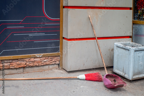 A broom and a dustpan on the sidewalk by the wall on a summer day
