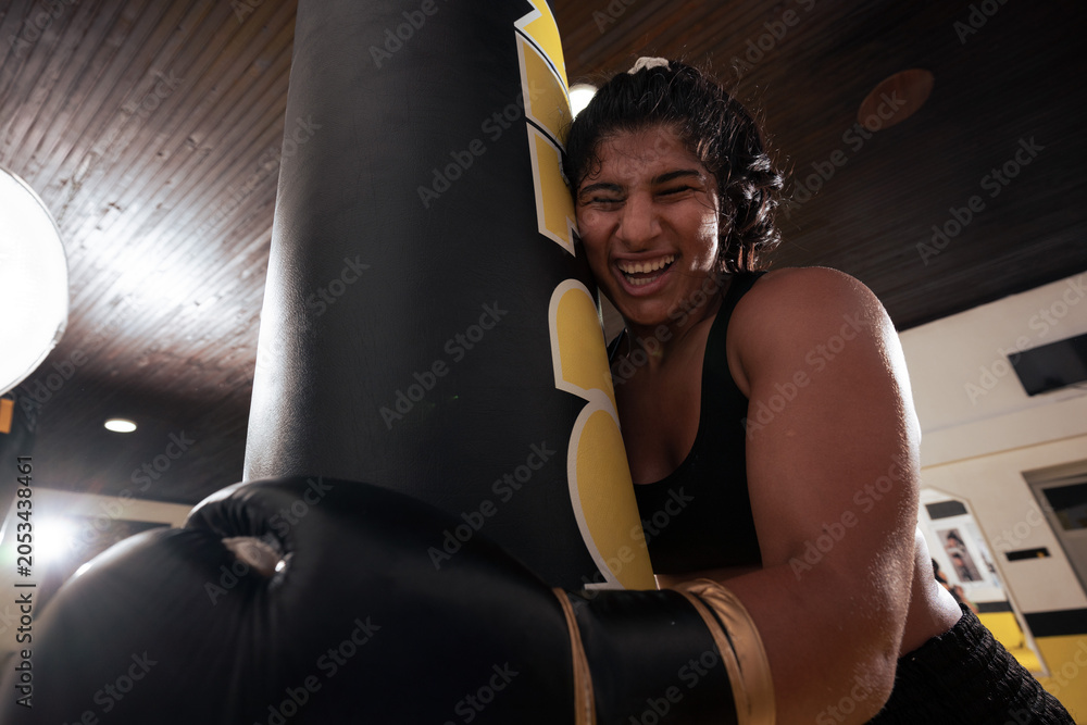 Naklejka premium Female Boxer Training With Heavy Bag In Gym Smiling After Intense Workout