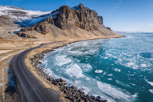 Rugged coastal road winds past icy sea and imposing mountain