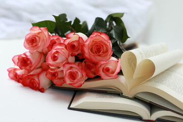 Romantic concept of love for reading with a fresh bouquet of pink roses and vintage open books with heart-shaped pages.