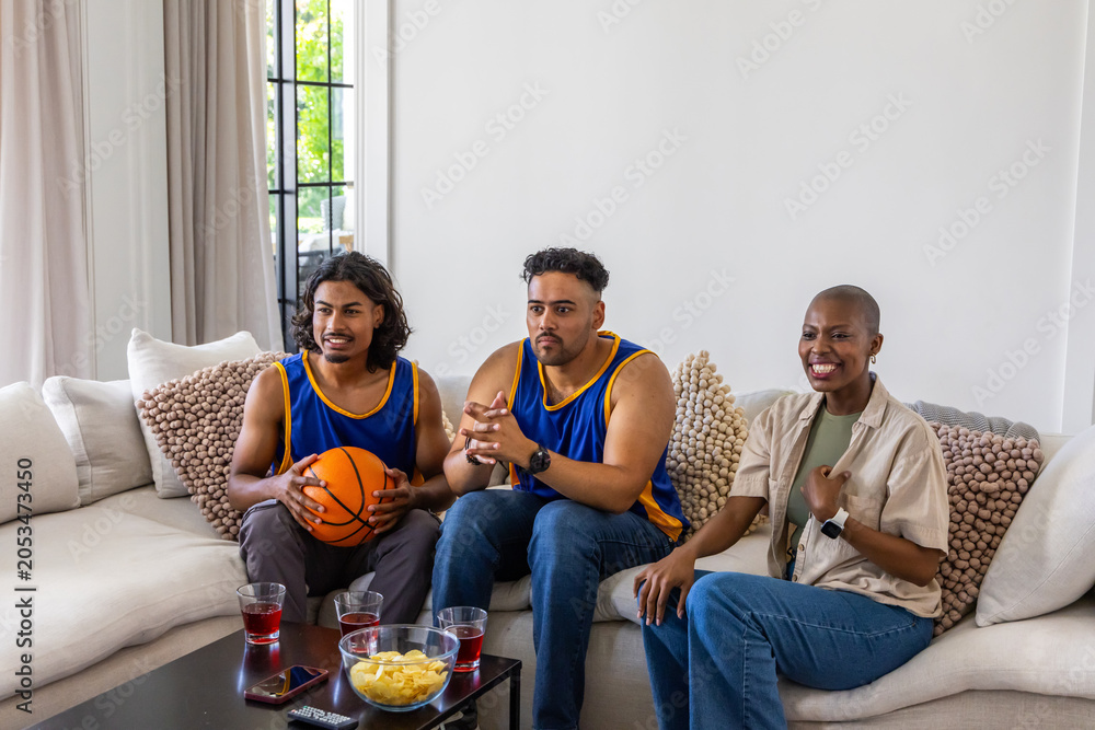 Naklejka premium Diverse friends wearing basketball jerseys watching game at home on couch with orange basketball