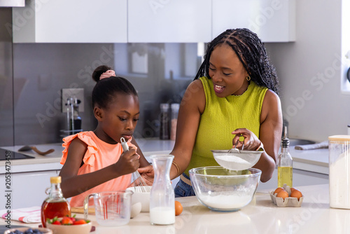 Fotografía African American mother and child sifting flour at kitchen island with sifter an